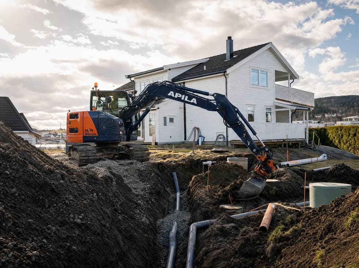 Apila gravemaskin graver drensgrøft ved en norsk bolig